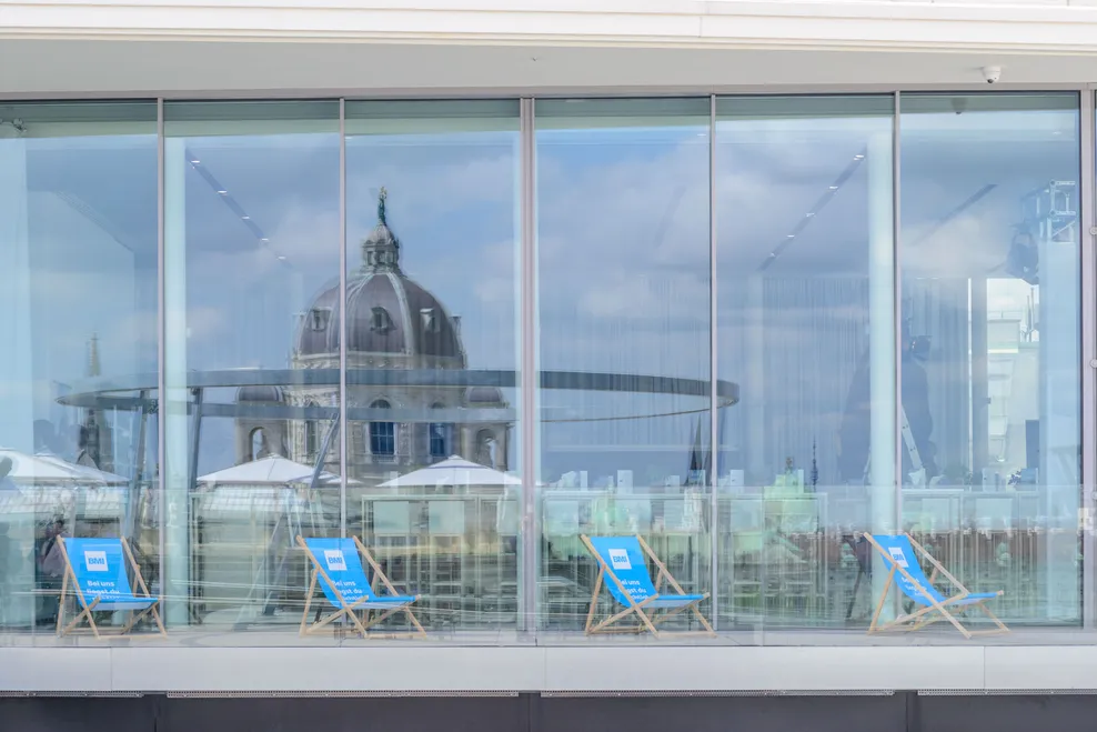 Strandliegen beim BMI Rooftop Talk 2022 bei der MQ Libelle spiegeln sich in den Fenstern des Hauses 