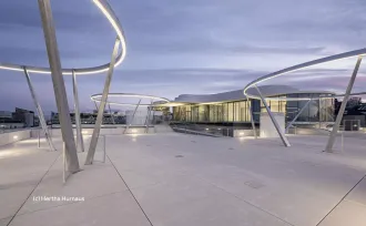 beleuchtete Dachterrasse der MC Libelle und Gebäude mit langer Glasfront dahinter 