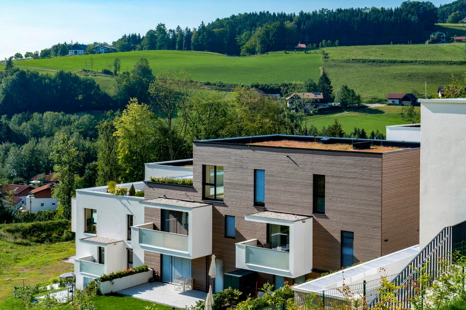 Haus mit Flachdach sowie Balkonen und Dachterrasse in flacher Lage und grüner Umgebung 