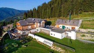 Das Almdorf Seinerzeit aus der Seitenperspektive zeigt mehrere Gebäude mit Steildächern sowie Flachdächern in einem einzigartigen Bergpanorama.