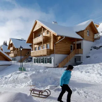 Rodeln am Katschberg bei verschneiten Häusern mit Holzfassade, Balkonen und Steildach im Hintergrund
