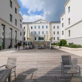 mehrere große weiße Wohngebäude mit schönem Platz zum Entspannen in der Mitte mit Stühlen, Sonnenschirmen und Pflanzen