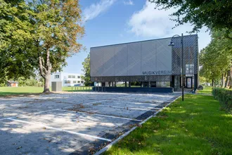 modernes Flachdach bei Turnsaal und Musikvereinshaus mit Parkplatz, alles unter einem Dach mit grauen Haus Fassade